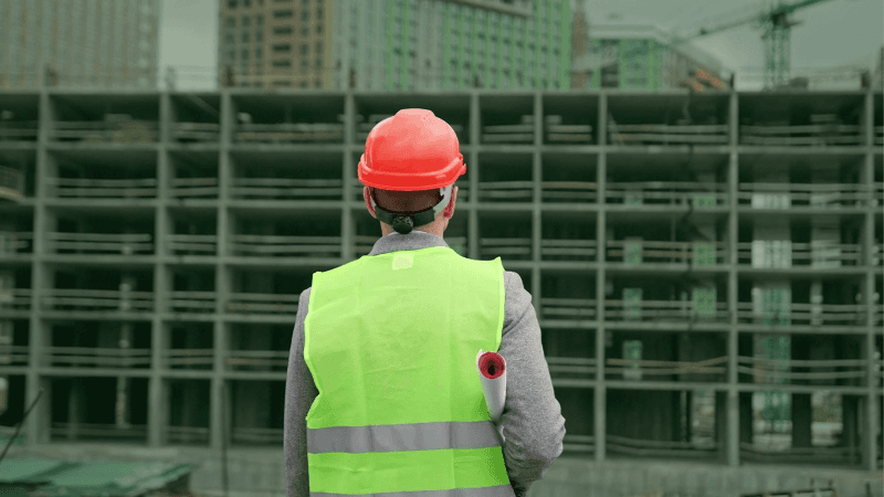 Construction Superintendent With Drawings Approaching New Building